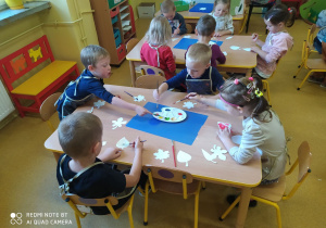 Dzieci przy stoliku malują liście.