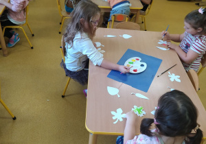 Dzieci przy stoliku malują liście.