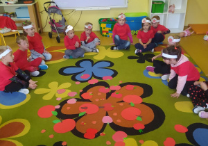 Dzieci siedzą kole na dywanie, po środku różnej wielkości jabłuszka wycięte z papieru.