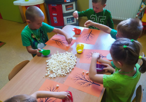 Dzieci przy stoliku wykonują drzewko z popcornu.