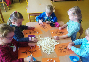 Dzieci przy stoliku wykonują drzewko z popcornu.