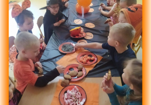 Dzieci przy stoliku częstują się smakołykami.