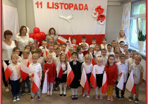 Dzieci z Sówek, Jeżyków i Lisków z paniami na tle biało-czerwonej dekoracji