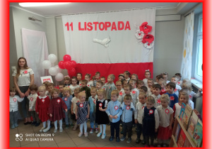 Dzieci na tle biało - czerwonej dekoracji 11 Listopada, odśpiewują Hymn
