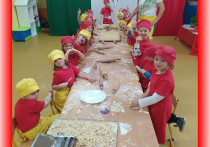 Dzieci ubrane w kucharskie stroje prezentują wykonany makaron.