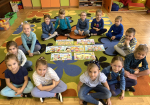 Dzieci siedzą na dywanie na którym rozłożone są karty z prawami dziecka