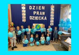 Dzieci ubrane na niebiesko z niebieskimi balonikami w niebieskiej ramce.