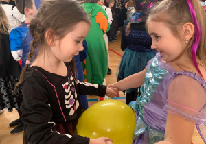 Dzieci w kolorowych przebraniach bawią się na udekorowanej balonami sali