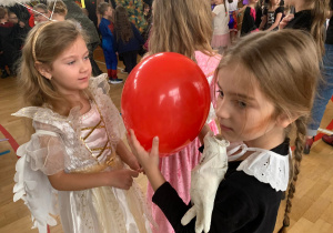 Dzieci w kolorowych przebraniach bawią się na udekorowanej balonami sali