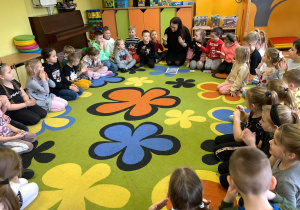 Grupa dzieci siedzi na dywanie,nauczyciel prezentuje język migowy.
