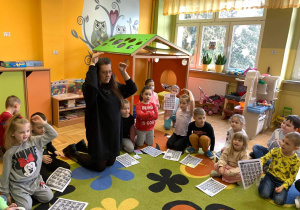 Grupa dzieci siedzi na dywanie,nauczyciel prezentuje język migowy.
