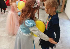 Para dziewczynek trzyma balona i tańczy.