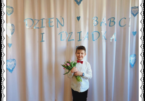 Chłopiec trzyma różowe tulipany. W tle napis Dzień Babci i Dziadka.
