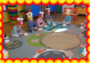 Dzieci siedzą na dywanie, wycinają. W środku leży papierowa pizza.