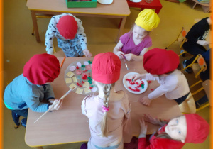 Dzieci przy stoliku wykonują prace plastyczną, pizze z papieru.