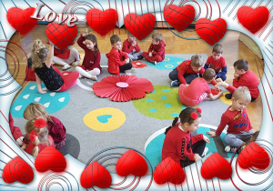 Dzieci siedzą na dywanie, przed nimi leżą ułożone z serduszek kwiaty