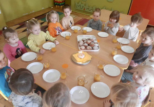 Dzieci siedzą przy stole na podwieczorku, przed nimi na tacy ułożone pączki