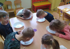 Dzieci przy stoliku bawią się w kotki i piją mleczko