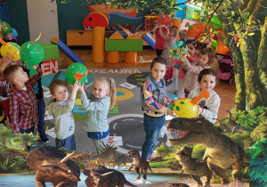 Zdjęcie w ramce z dinozaurami. Dzieci bawią się wykonanymi z balonów dinozaurami