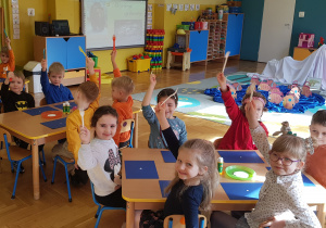 Dzieci siedzą przy stolikach, trzymają plastikowe widelce.
