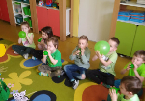 Dzieci na dywanie dmuchają zielone balony - ćwiczenia oddechowe