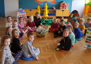 Dzieci siedzą na podłodze, w środku koszyczek z prezentami.