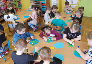 Dzieci siedzą przy stolikach, wykonują prace plastyczne.