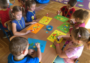 Dzieci wyklejają kolorowymi kółkami sylwetę jeża.