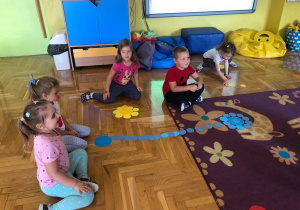 Dzieci układają na podłodze kwiatka z kolorowych kółek