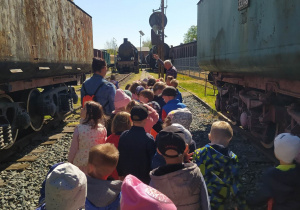 Dzieci idą ścieżką wśród starych lokomotyw