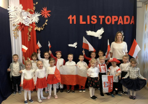 Dzieci ubrane na biało-czerwono z panią Olą na tle dekoracji patriotycznej