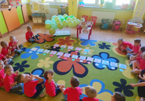 Dzieci w kole, zabawa w kodowanie kolorami napisu Dzień Przedszkolaka.