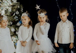 Dziewczynki przebrane za śnieżynki i chłopiec w galowym stroju stoją podczas występu
