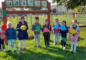 Dzieci w ogrodzie przedszkolnym z kolorowymi kropkami w dłoniach.