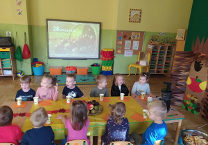 Dzieci siedzą przy stoliku, w tle napis 28 września i kosz jabłek