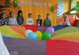 Dzieci trzymają kolorową chustę z balonami.