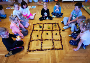 Grupa dzieci gra w "kółko i krzyżyk" wykonane z naturalnych okazów.