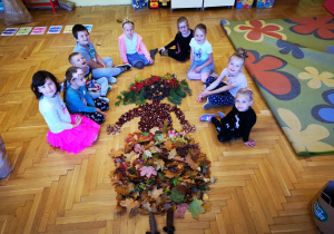 Dzieci siedzą a przed nimi Pani Jesień wykonana z darów przyrody.