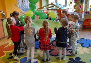 Dzieci podrzucają na materiale zielone balony.