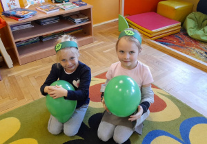 Maja i Jula w opaskach na głowie siedzą na dywanie trzymając balony.
