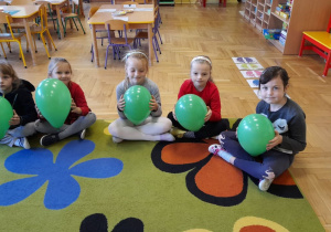 Dzieci siedzą na dywanie, każde trzyma swój balonik.