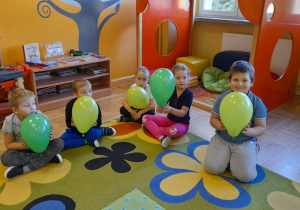 Dzieci siedzą na dywanie. trzymając w rączkach balony.