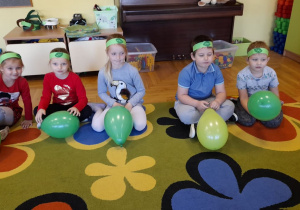 Dzieci siedzą na dywanie z balonami w rączkach.