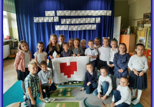 Dzieci na tle granatowego materiału z napisem Dzień Edukacji Narodowej z sercem na tablicy do kodowania